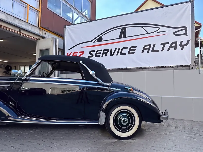 Klassisches dunkelblaues Mercedes-Benz-Cabriolet mit Weißwandreifen und geschlossenem Verdeck vor dem Werkstatt-Banner